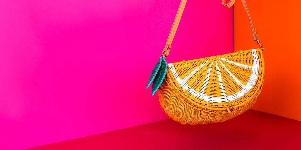 Wicker Darling orange purse orange shaped handbag hands in a colourful red, pink and orange background.