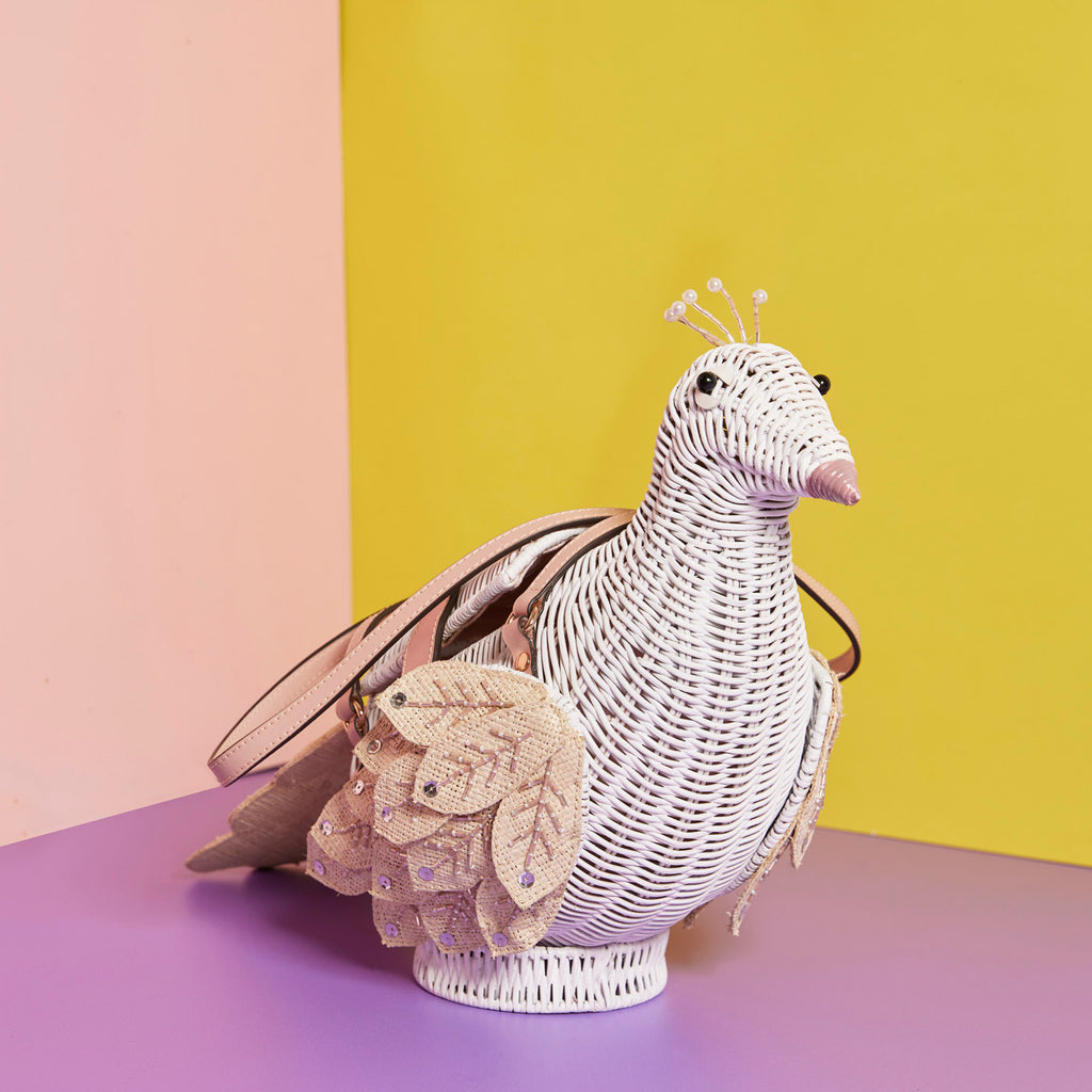 Wicker Darling persephone white peacock bag bird shaped bag sits in a colourful background