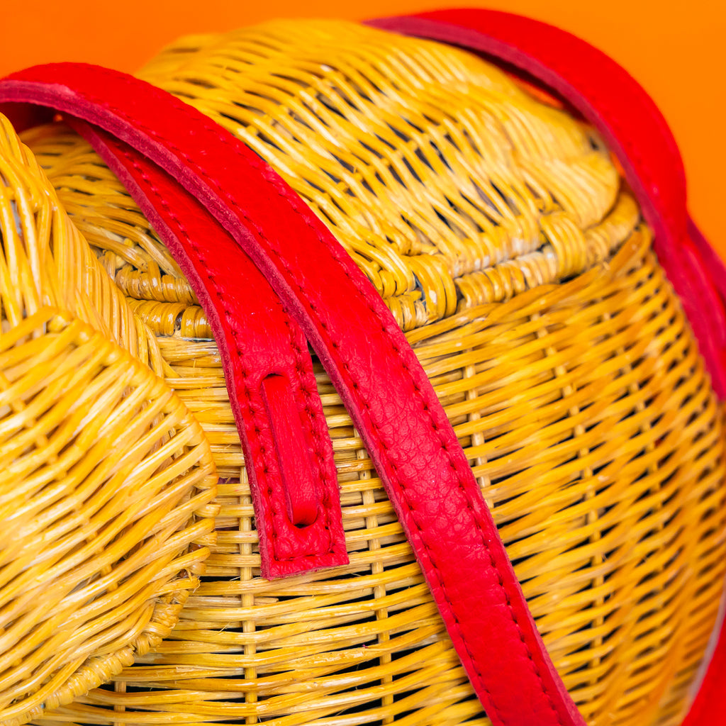 A close up of the woven rattan and red leather handles on an elephant shaped wicker handbag.