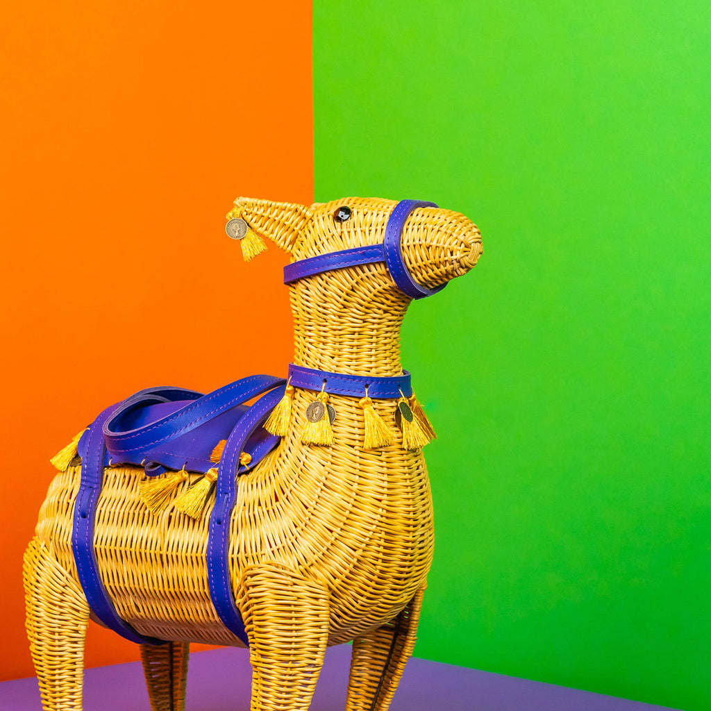 Wicker darling yellow llama shaped bag with purple detailing sits in a colourful room