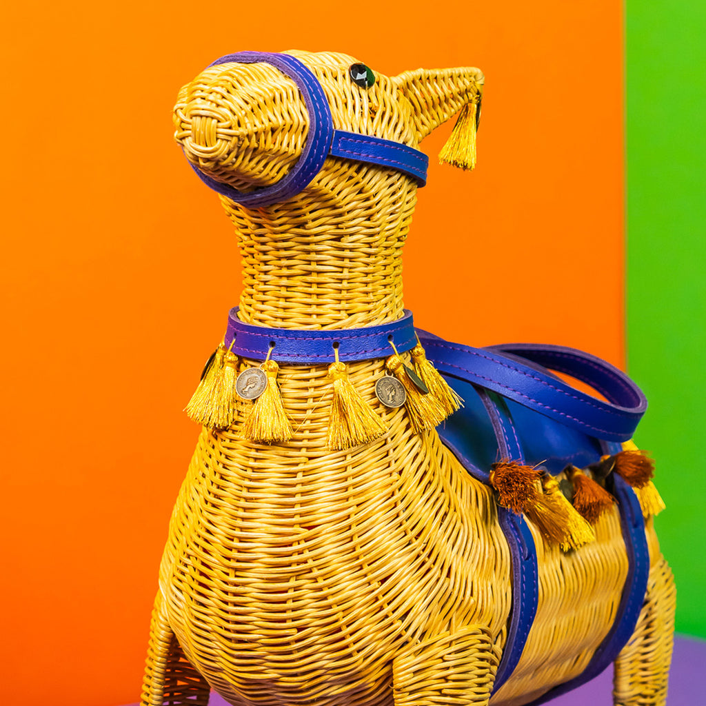 Wicker darling yellow llama shaped bag with purple detailing sits in a colourful room