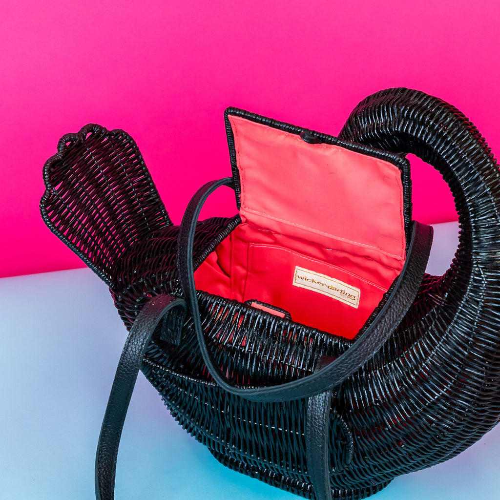 Wicker darling Odile the black swan purse swan handbag sits in a colourful background.