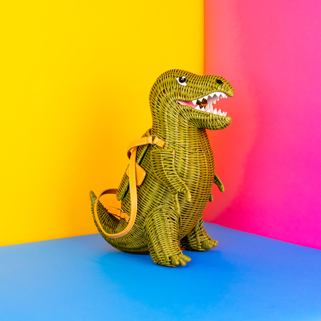 A wicker t-rex dinosaur handbag standing on two legs, mouth open. It looks like it's smiling. It has rows of white leather teeth.
