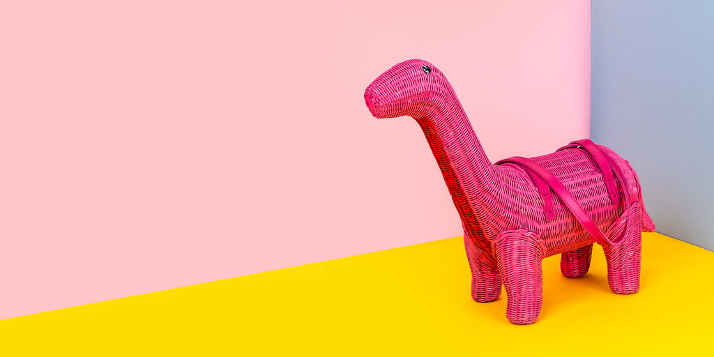 Wicker Darling anne the pink brontesaurus cute dinosaur shaped purse sits in a colourful background