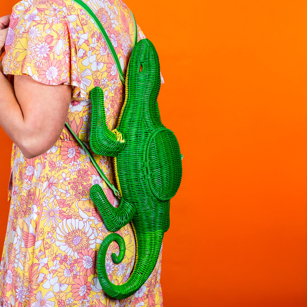 Wicker darling green lizard handbag lizard purse is worn by a woman in a floral dress in front of an orange background.