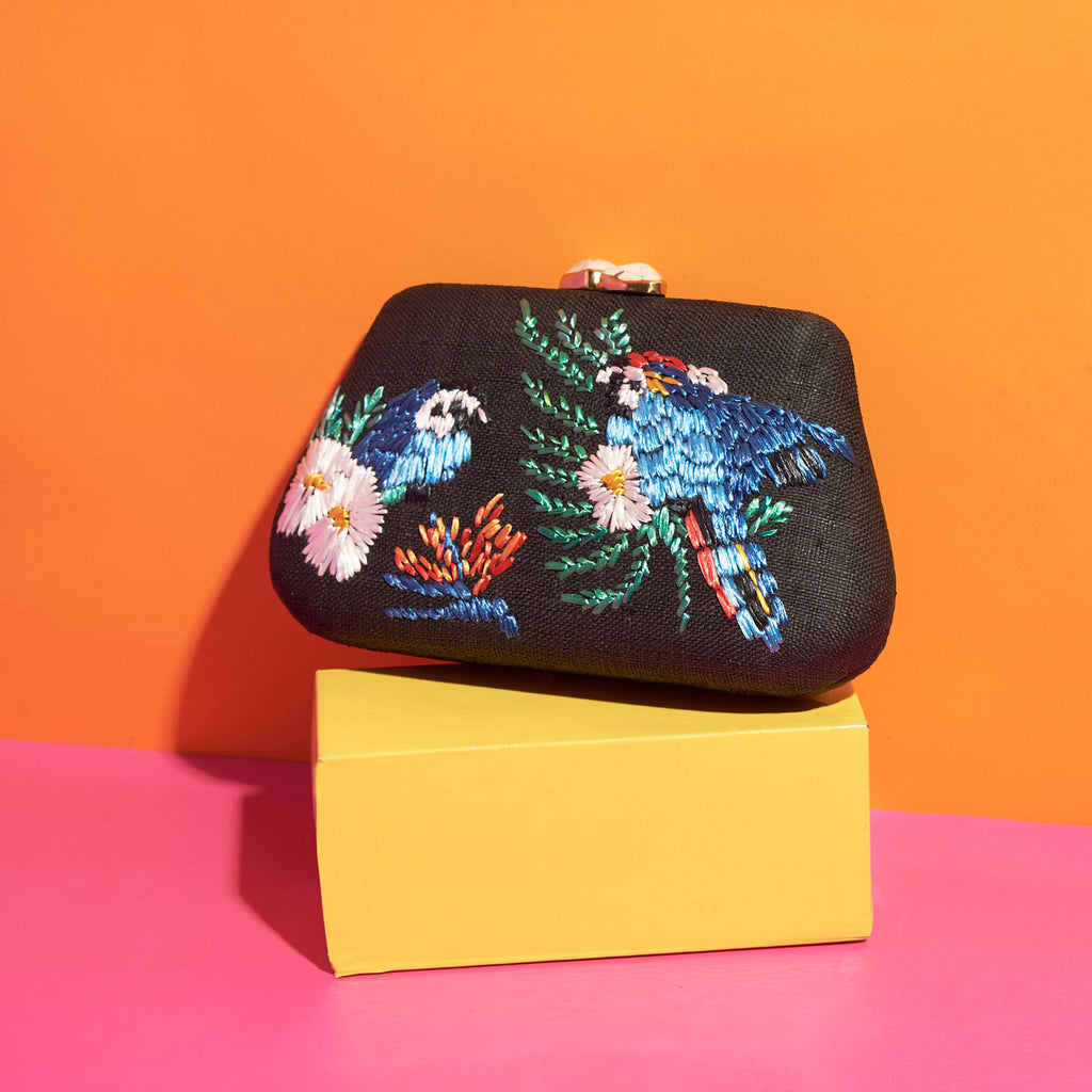 Wicker Darling black fabric clutch bag macaw bag sits in a colourful background