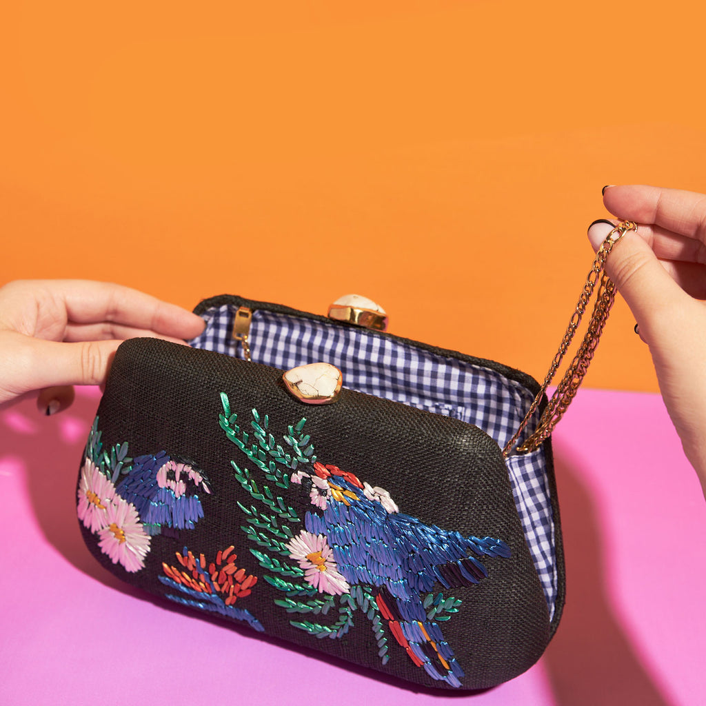 Wicker Darling black fabric clutch bag macaw bag sits in a colourful background