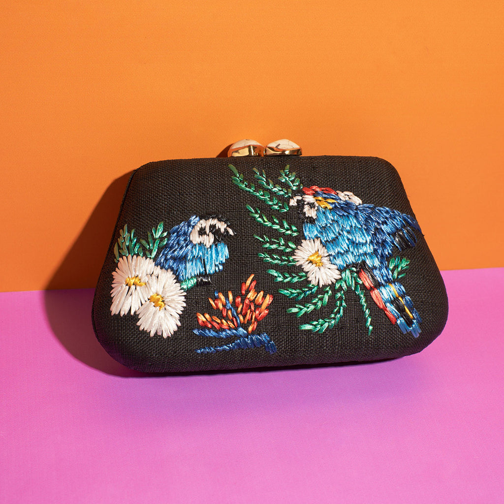 Wicker Darling black fabric clutch bag macaw bag sits in a colourful background