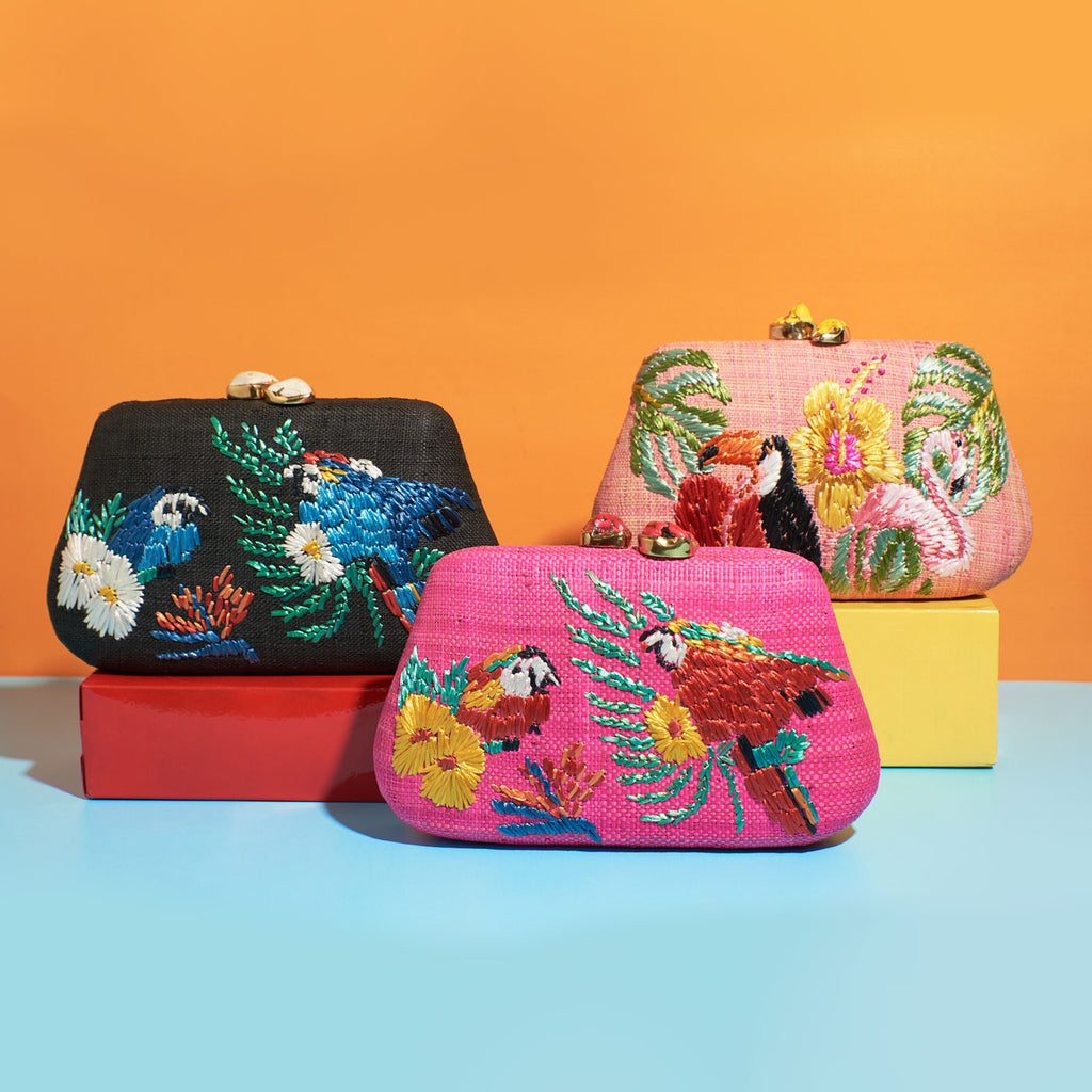 Wicker Darling hot pink fabric clutch bag macaw bag sits in a colourful background