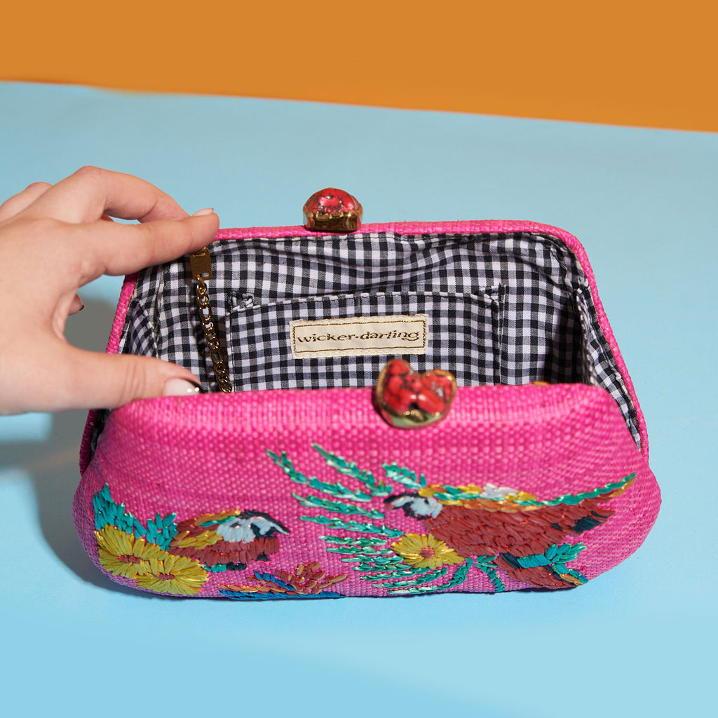 Wicker Darling hot pink fabric clutch bag macaw bag sits in a colourful background