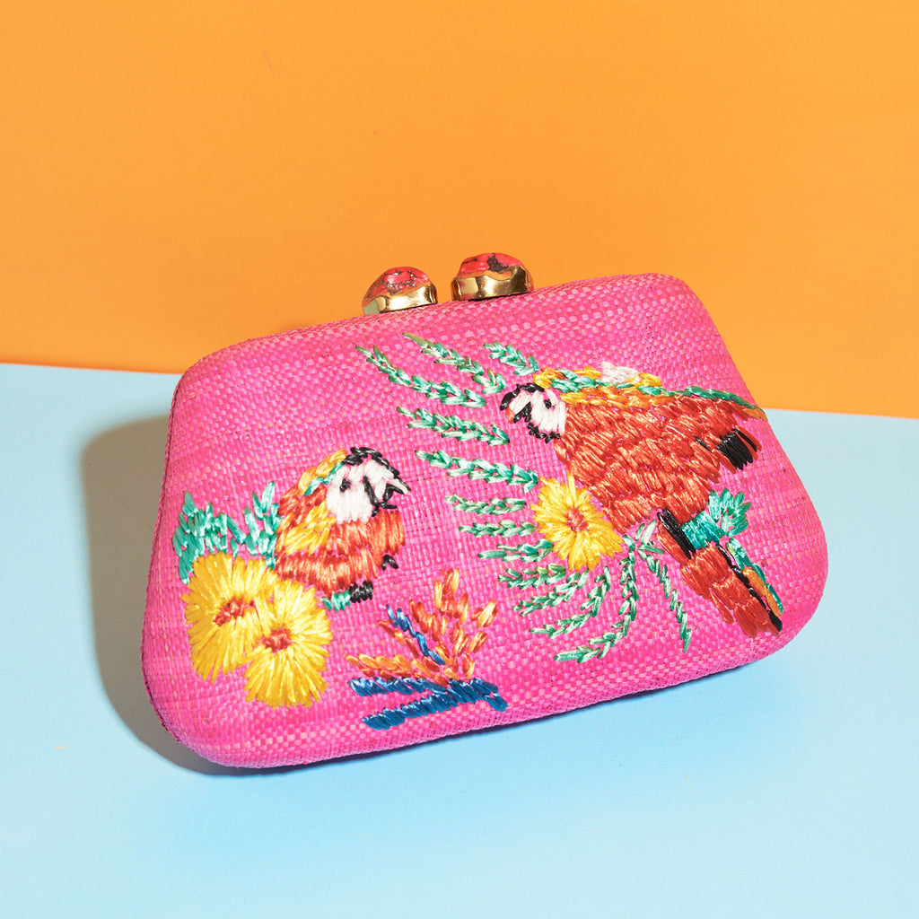 Wicker Darling hot pink fabric clutch bag macaw bag sits in a colourful background