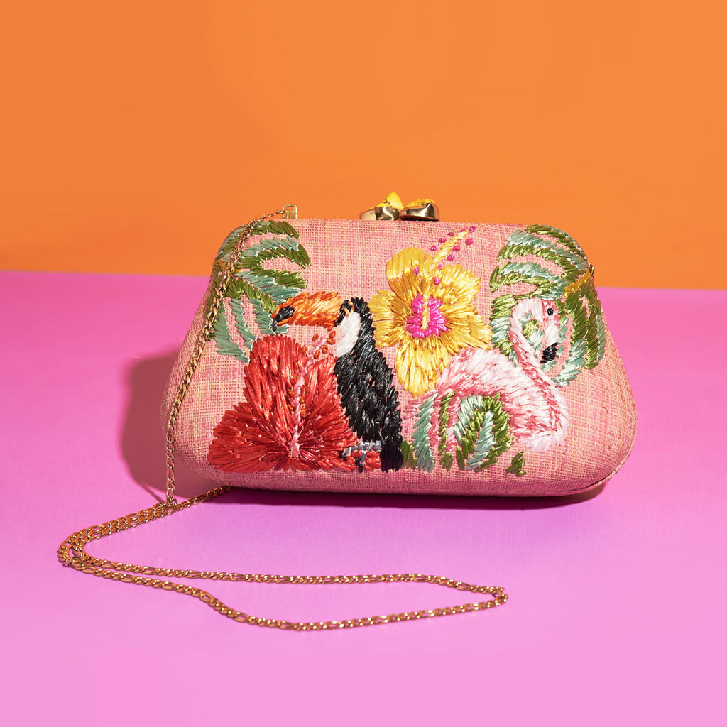 Wicker Darling light pink tropicana clutch purse toucan bag flamingo bag sits on a colourful background
