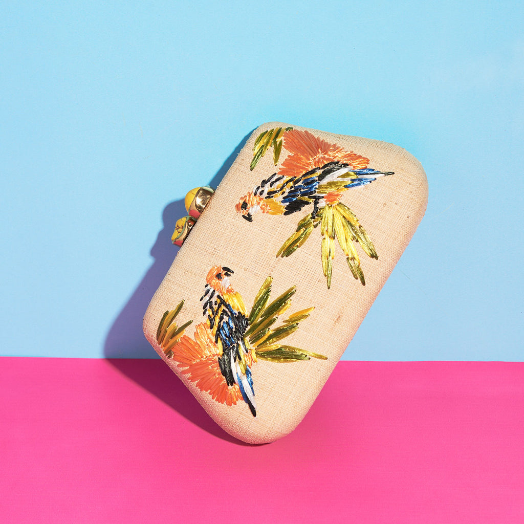 Wicker Darling natural fabric clutch bag macaw bag sits in a colourful background