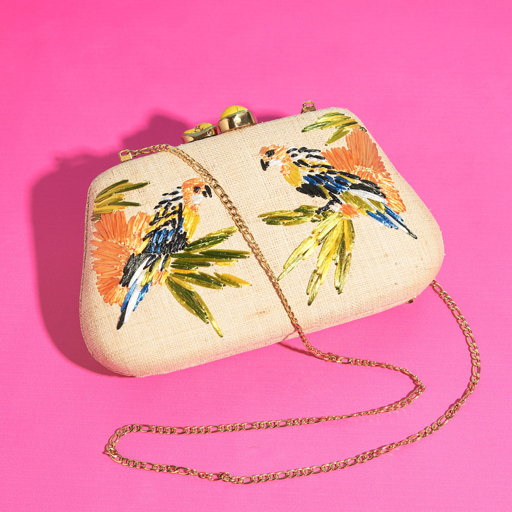 Wicker Darling natural fabric clutch bag macaw bag sits in a colourful background