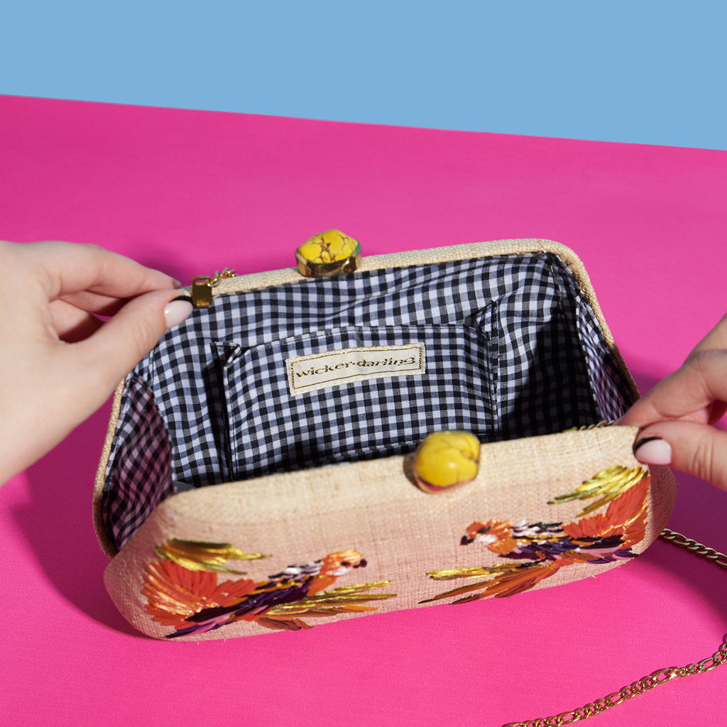 Wicker Darling natural fabric clutch bag macaw bag sits in a colourful background