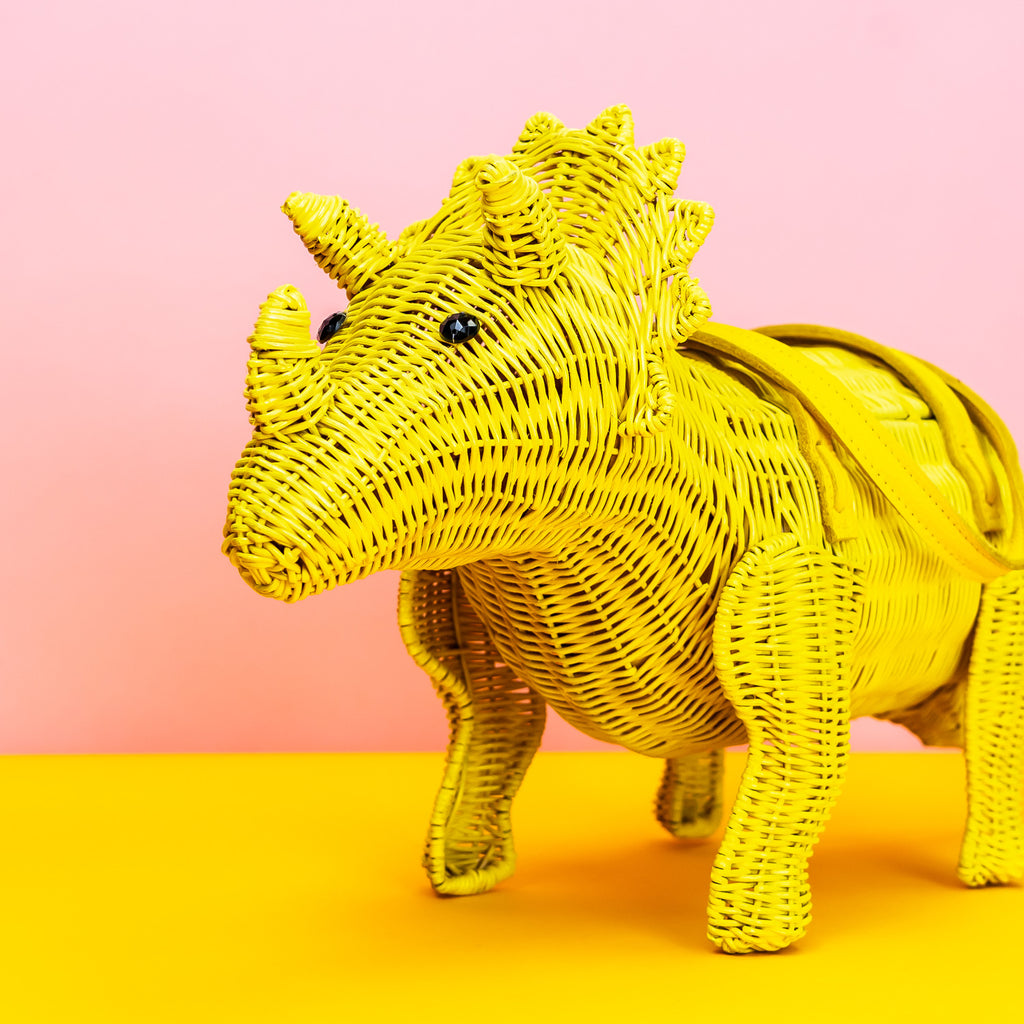 Wicker Darling yellow Ellie triceratops cute dinosaur bag sits in a colourful background