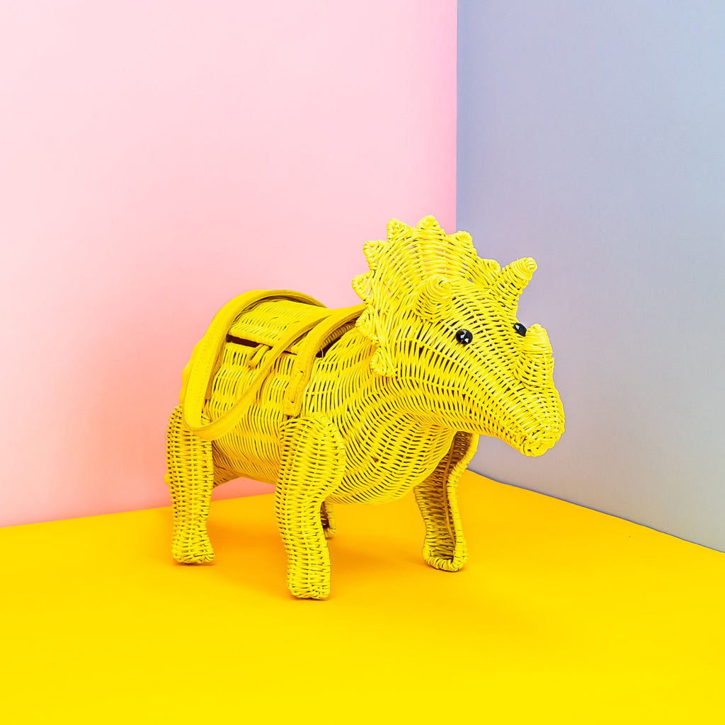 Wicker Darling yellow Ellie triceratops cute dinosaur bag sits in a colourful background