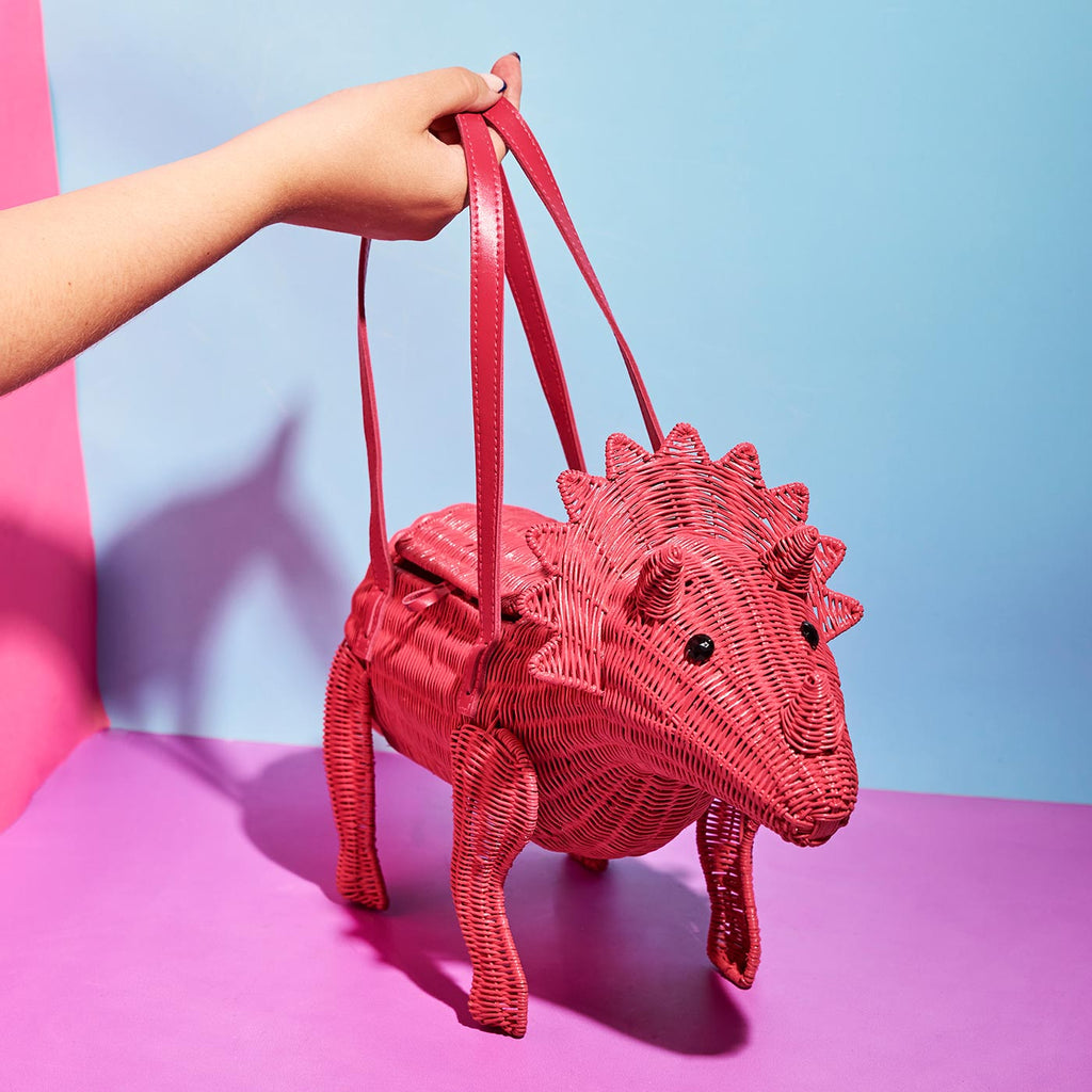 Wicker darling joan Triceratops pink cute dinosaur bag sits in a colourful background
