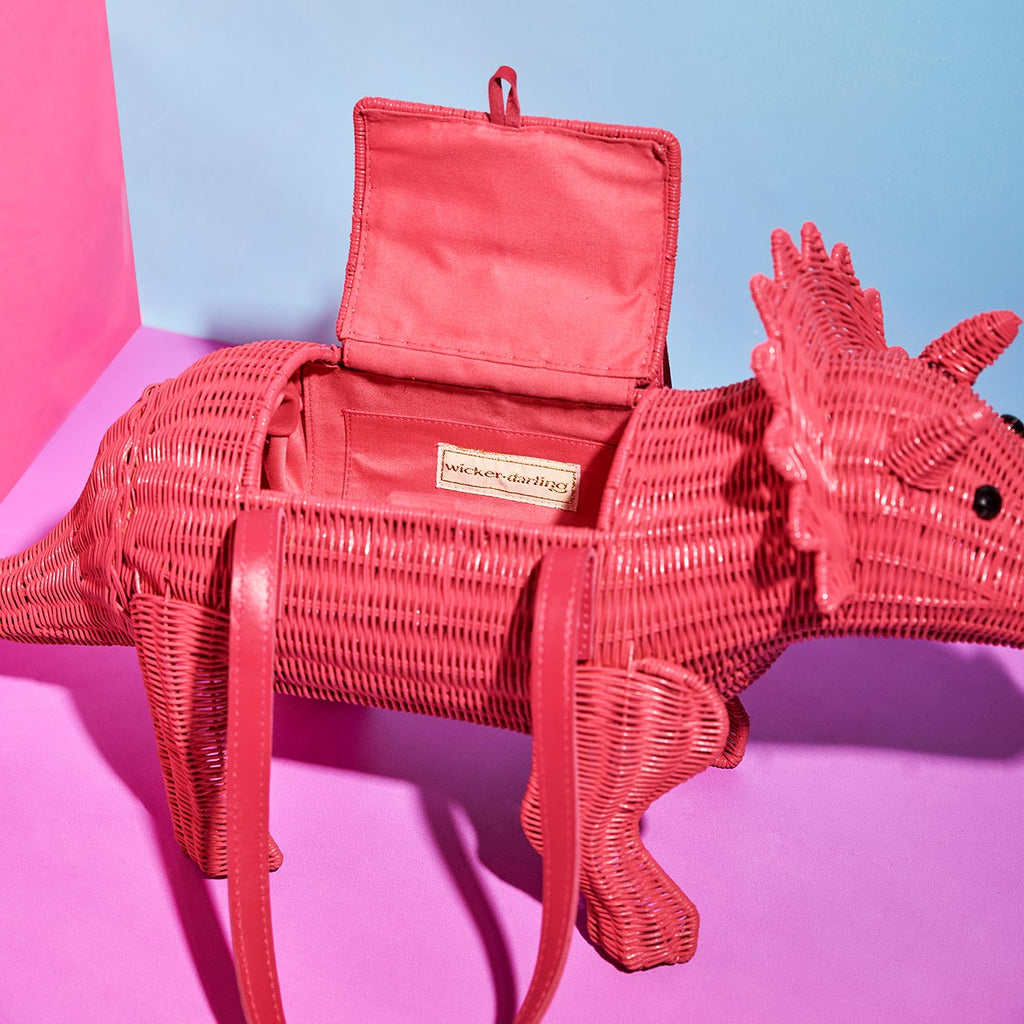 Wicker darling joan Triceratops pink cute dinosaur bag sits in a colourful background
