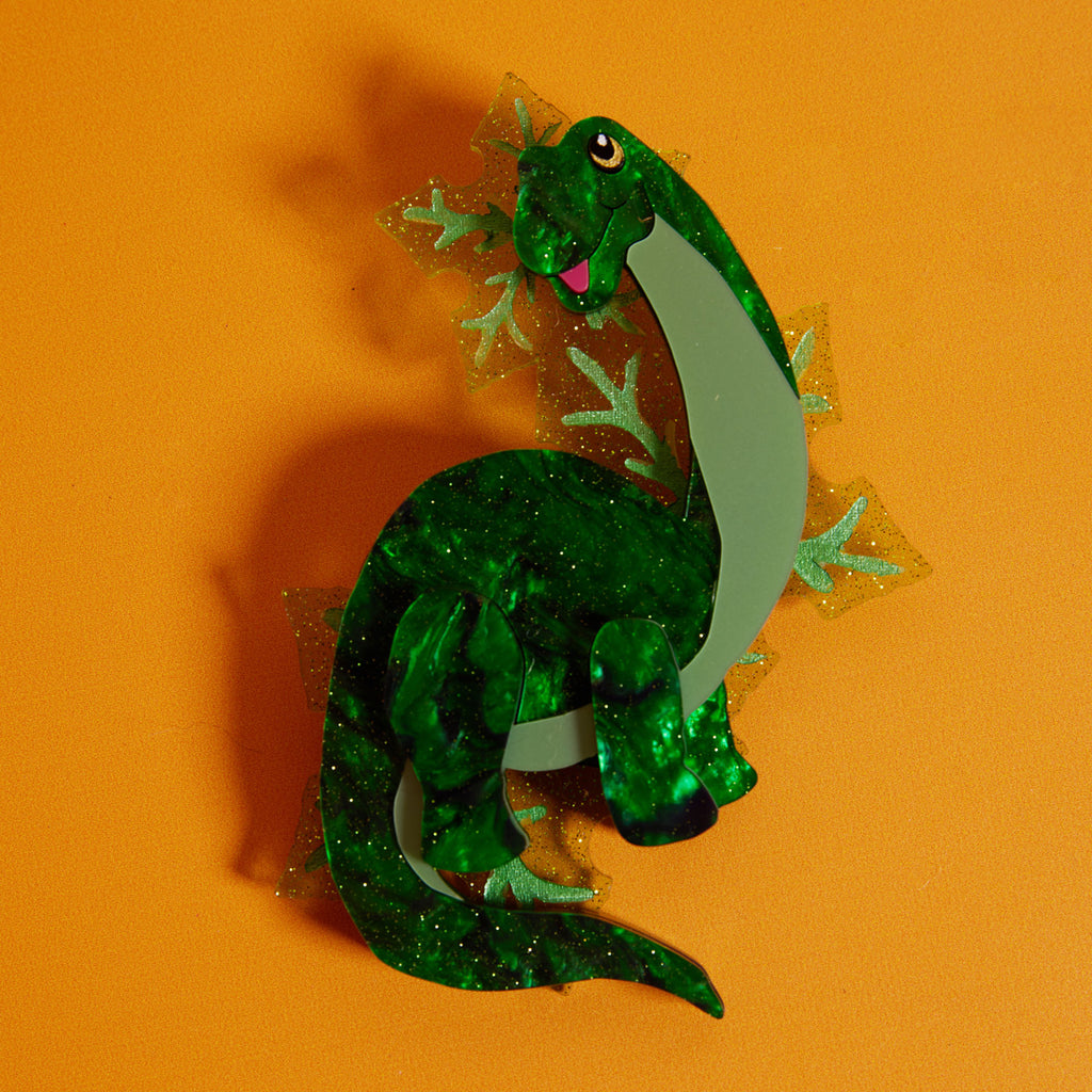 Wicker Darling What Willow Did collab dinosaur brooch sits in a colourful background