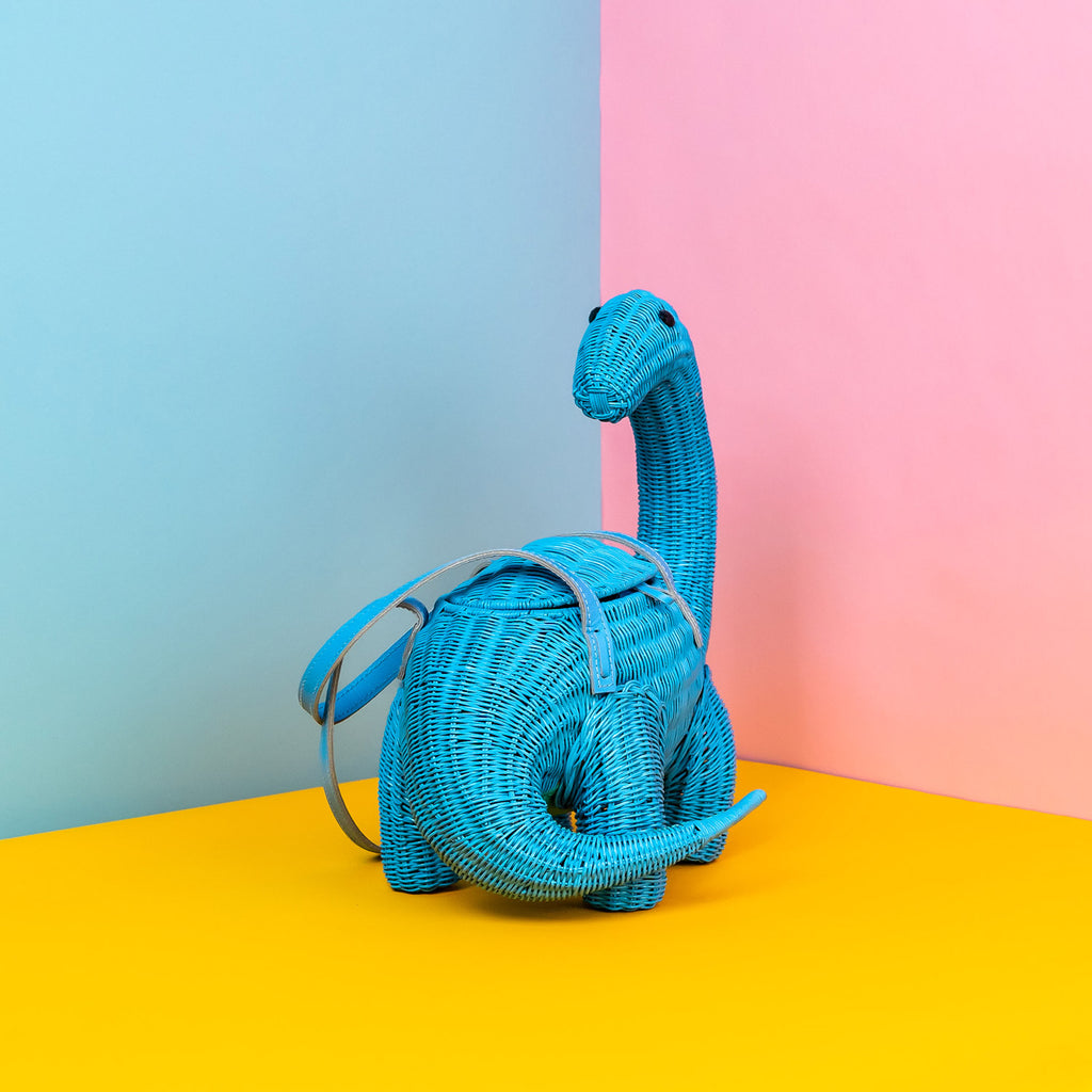 Wicker Darling blue brontesaurus purse dinosaur shaped bag sits in a colourful background